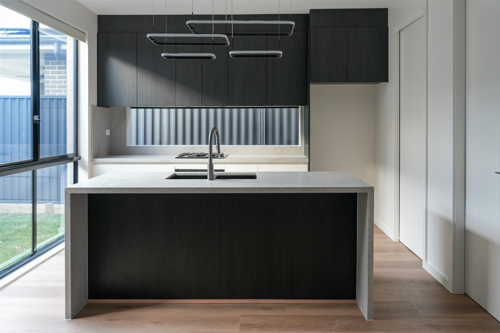 Kitchen with stone island bench, black joinery and pendant lighting in one of the dual-occupancy homes in Sydney's North West